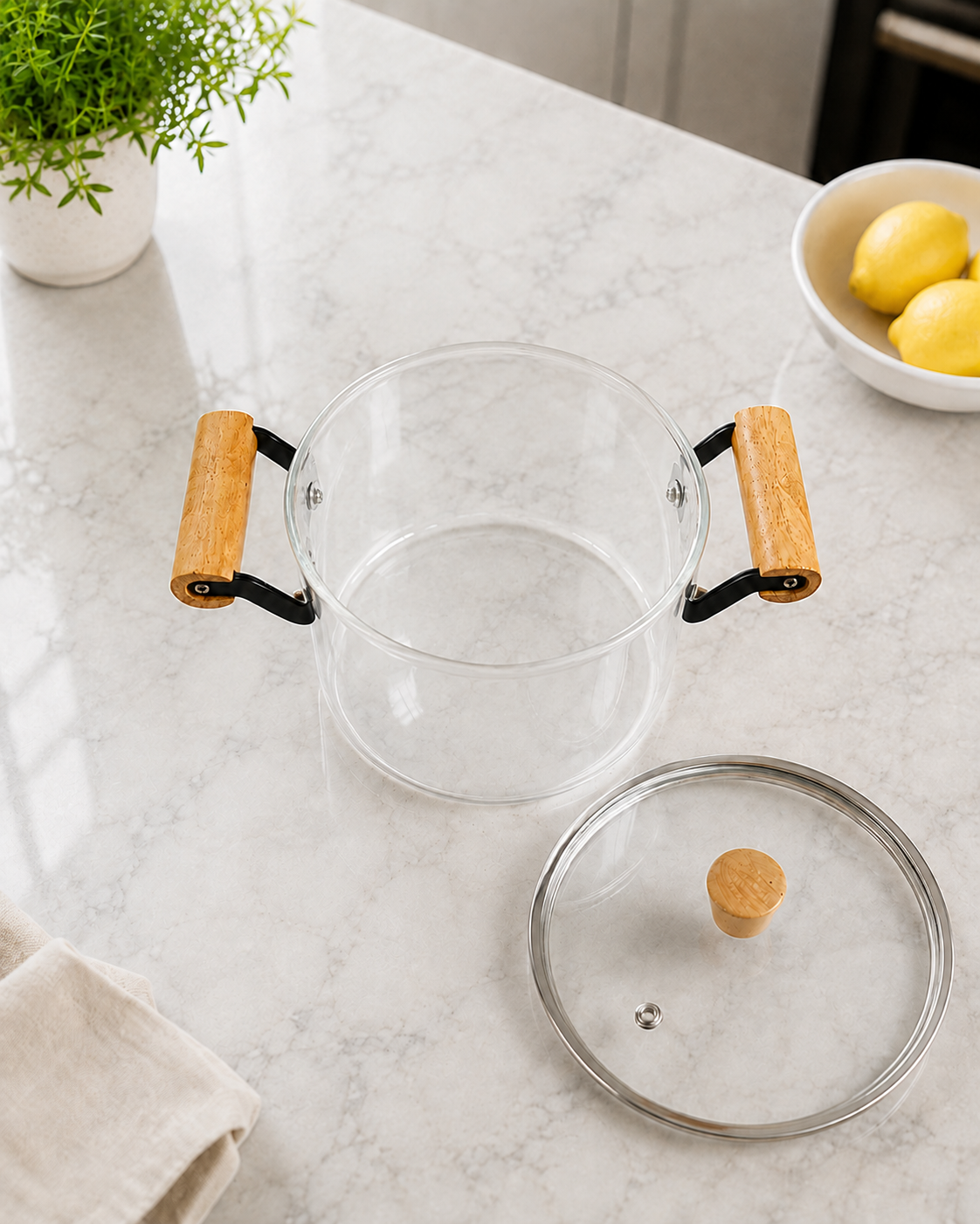Olla de vidrio de borosilicato con asas de madera, destapada, con tapa apoyada sobre mesada de mármol